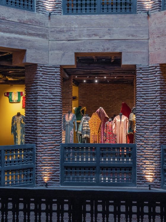 Caftanes marroquíes históricos expuestos en las galerías de columnas de ladrillo de un museo.