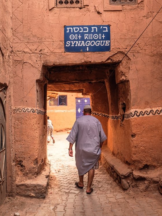 Una calle de kasbah de adobe con un cartel en hebreo, árabe e inglés que señala una sinagoga.